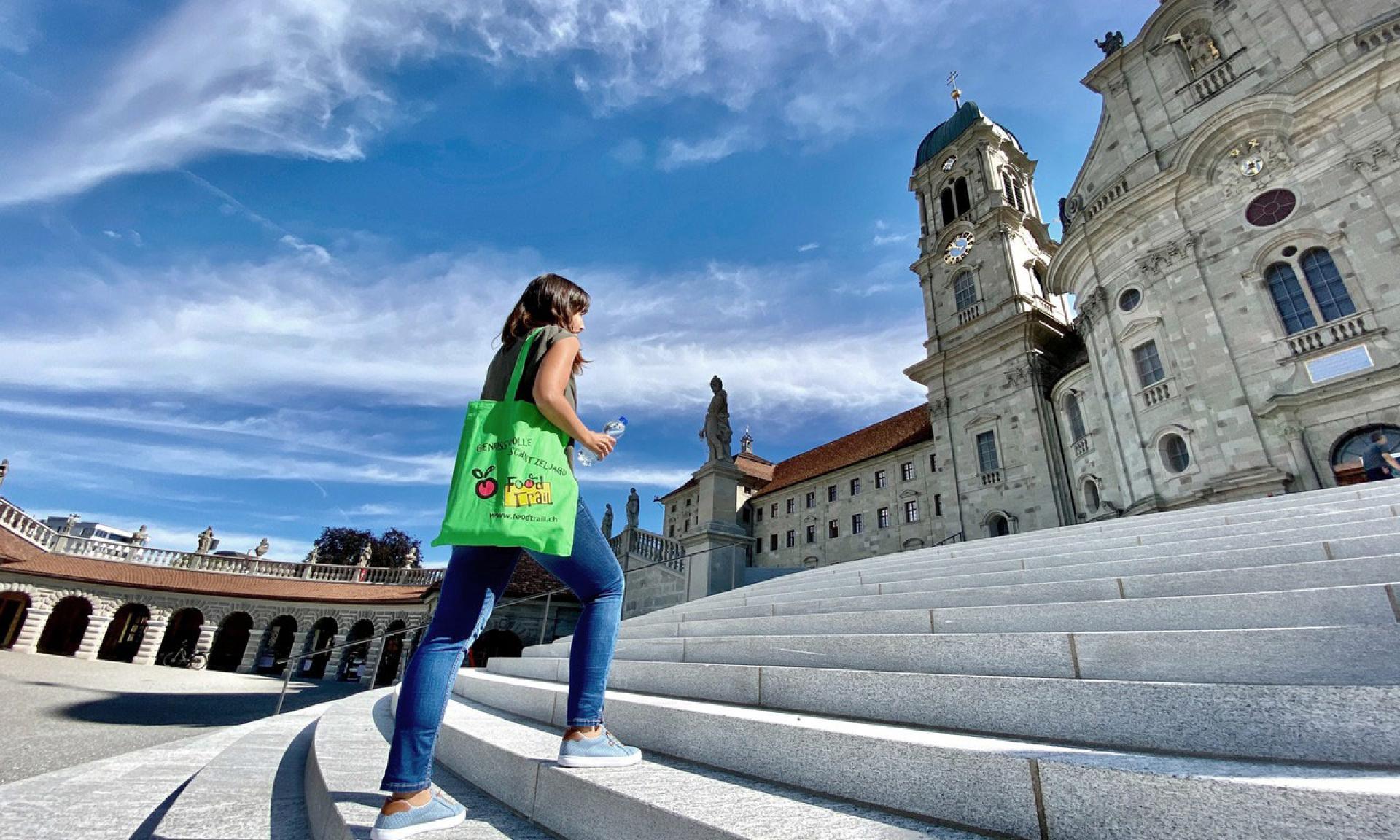 Eine Frau unterwegs auf dem FoodTrail auf der Treppe vor dem Kloster Einsiedeln. 